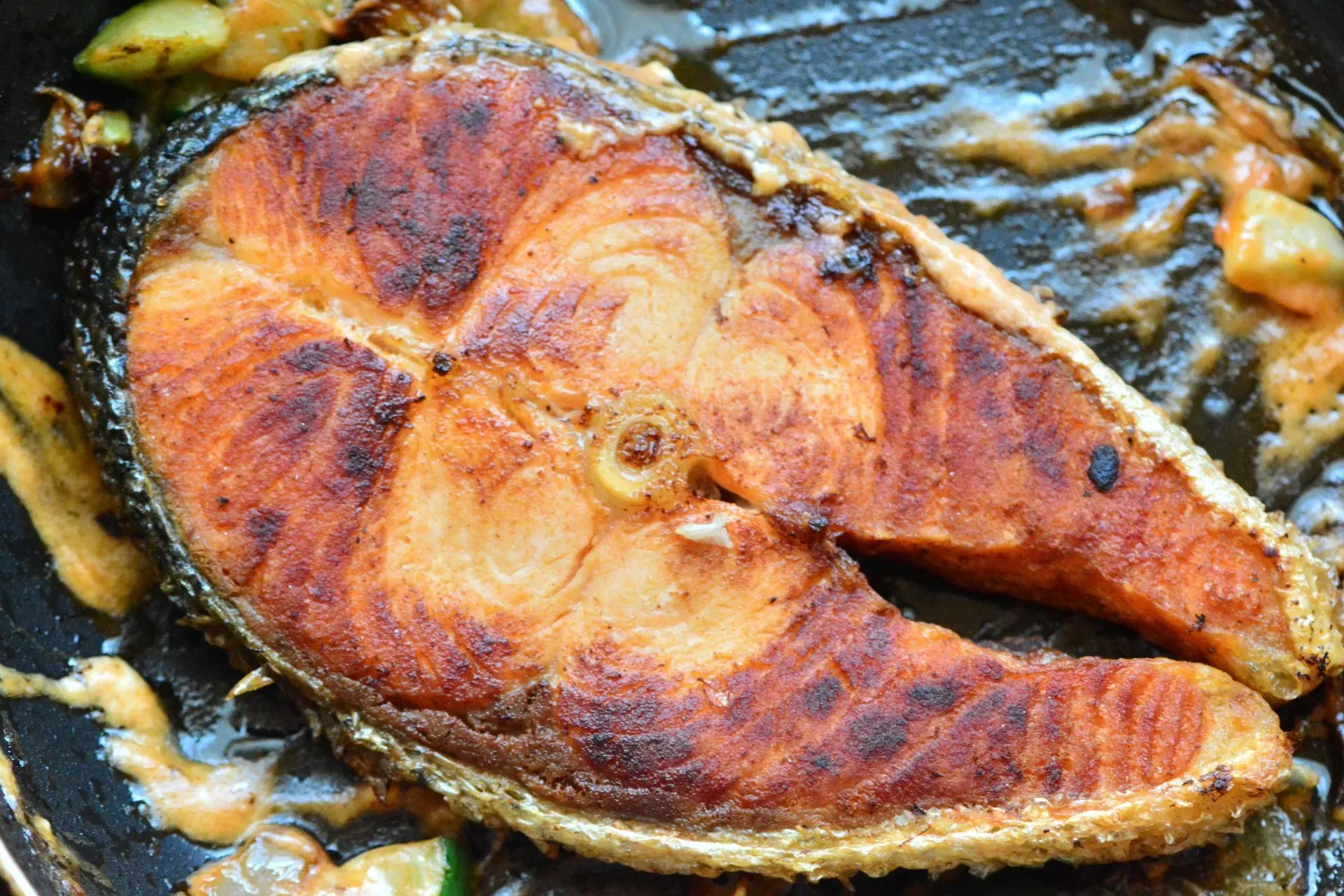 A large piece of salmon is being cooked in a frying pan.