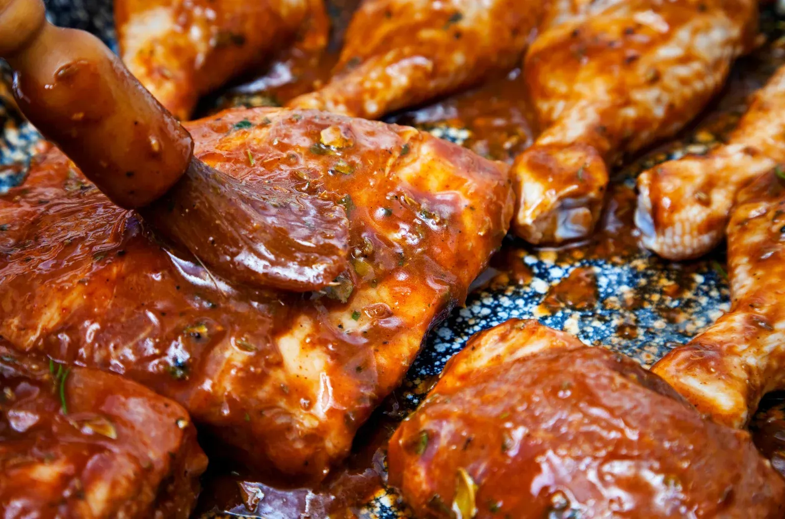 A close up of a person applying sauce to chicken in a pan.