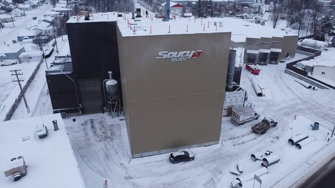 Vue aérienne d'un bâtiment industriel enneigé portant le logo « SCA », entouré d'un sol enneigé et d'autres structures.