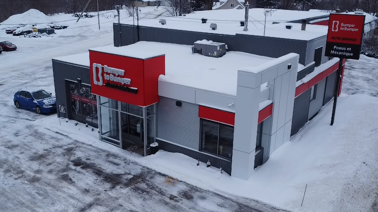 Le bâtiment du garage Boucher en hiver. Façade rouge et grise, toit et alentours enneigés.