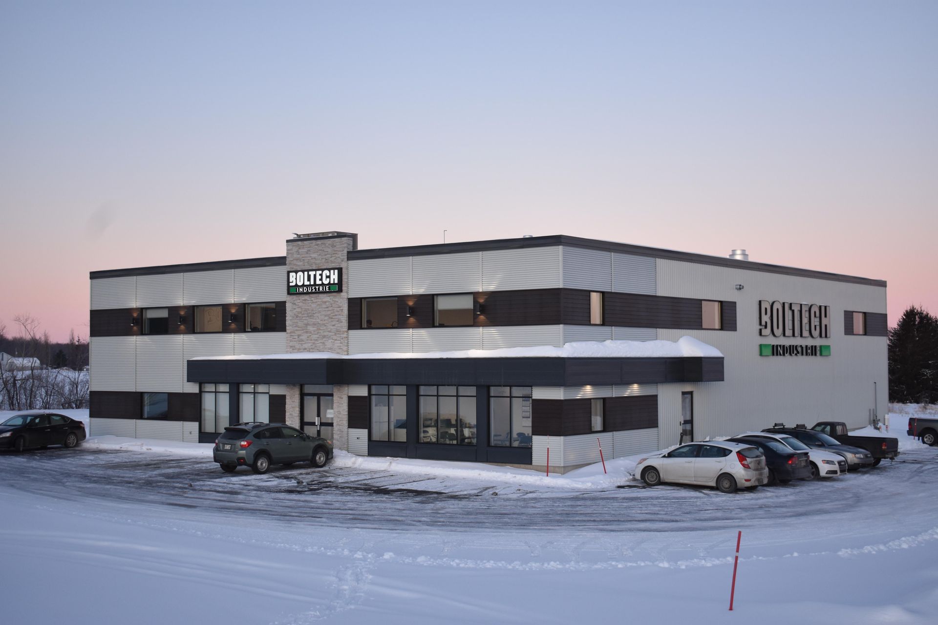 Immeuble de bureaux moderne de deux étages avec sol enneigé, voitures garées et logo « FONTEK » visible.