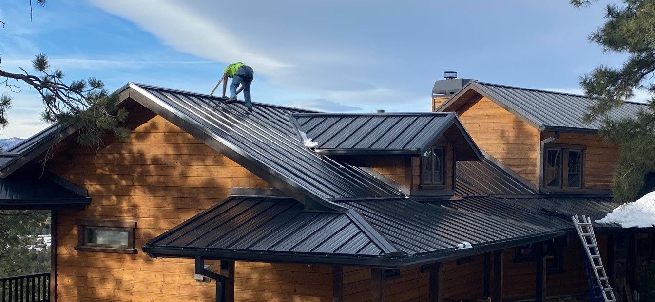 Man is standing on top of a wooden house with a metal roof – Evergreen, CO - Elevated Roofing