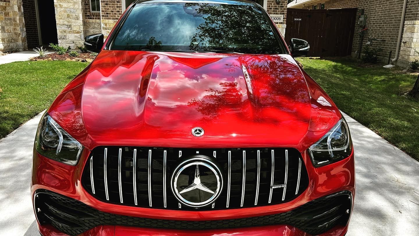 Red Mercedes-Benz SUV with black grill, parked on driveway, sunlight reflecting on the hood.