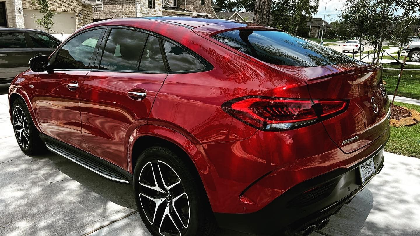 Red Mercedes-Benz GLE Coupe parked on a concrete driveway in a sunny residential setting.