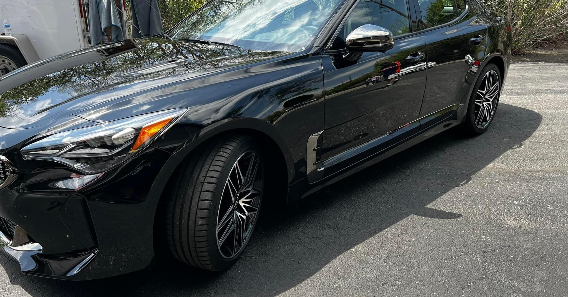 Black Kia Stinger sports car parked on asphalt, shiny paint, black rims, sunny outdoors.