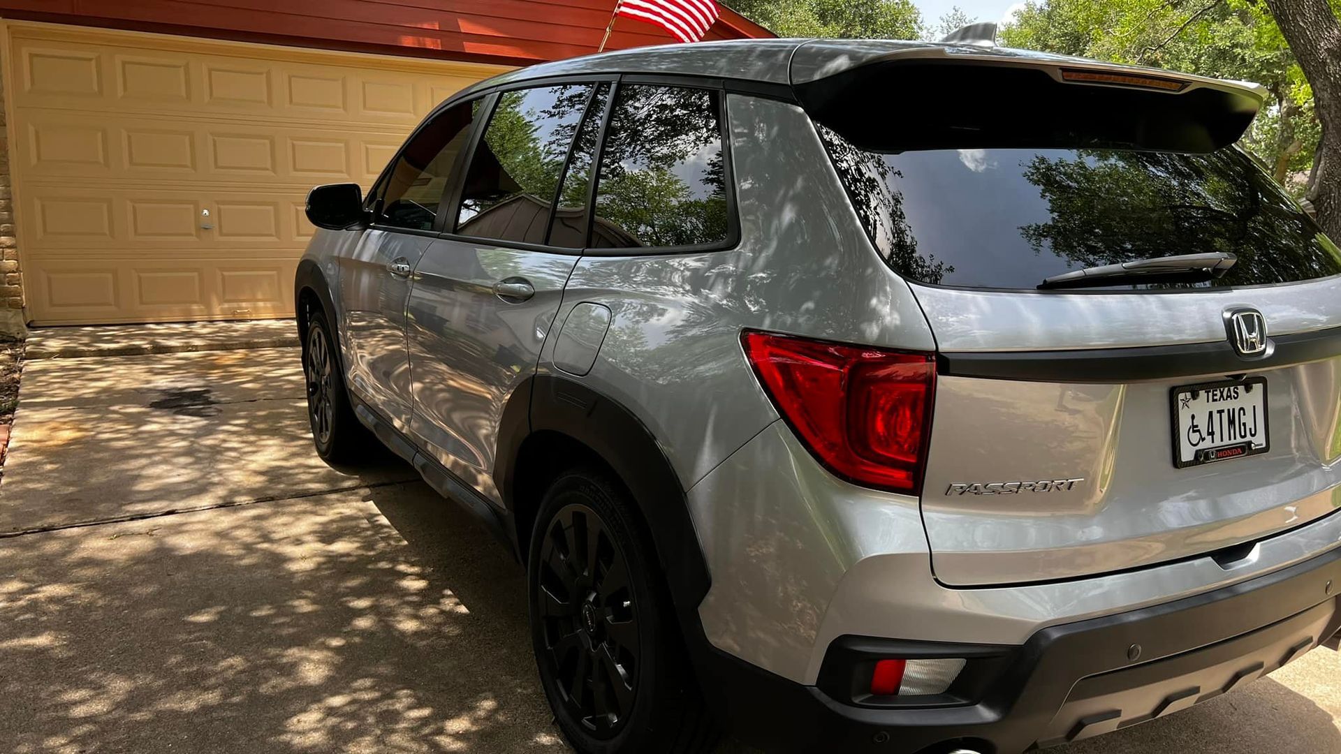 Silver Honda Passport SUV parked on a driveway in front of a tan garage.
