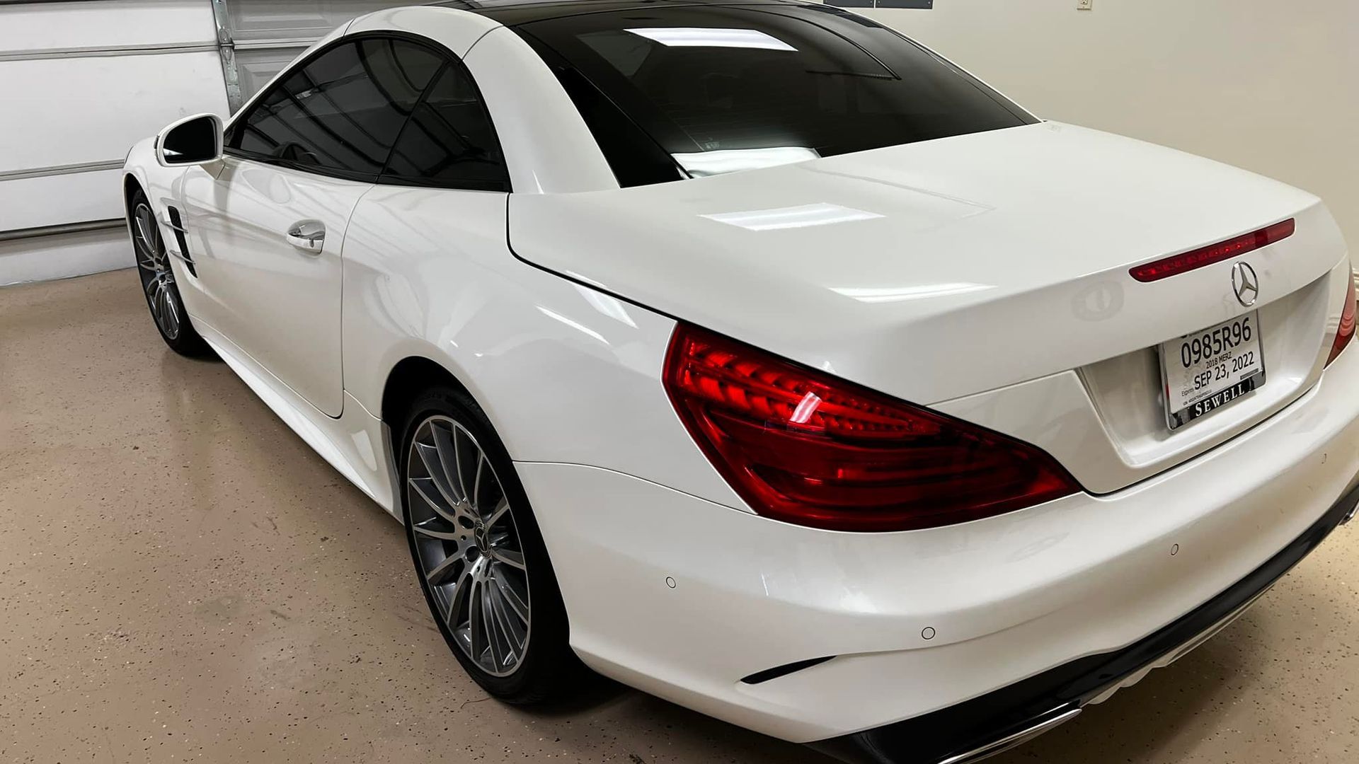 White Mercedes-Benz SL-Class convertible with black top, parked inside a garage.