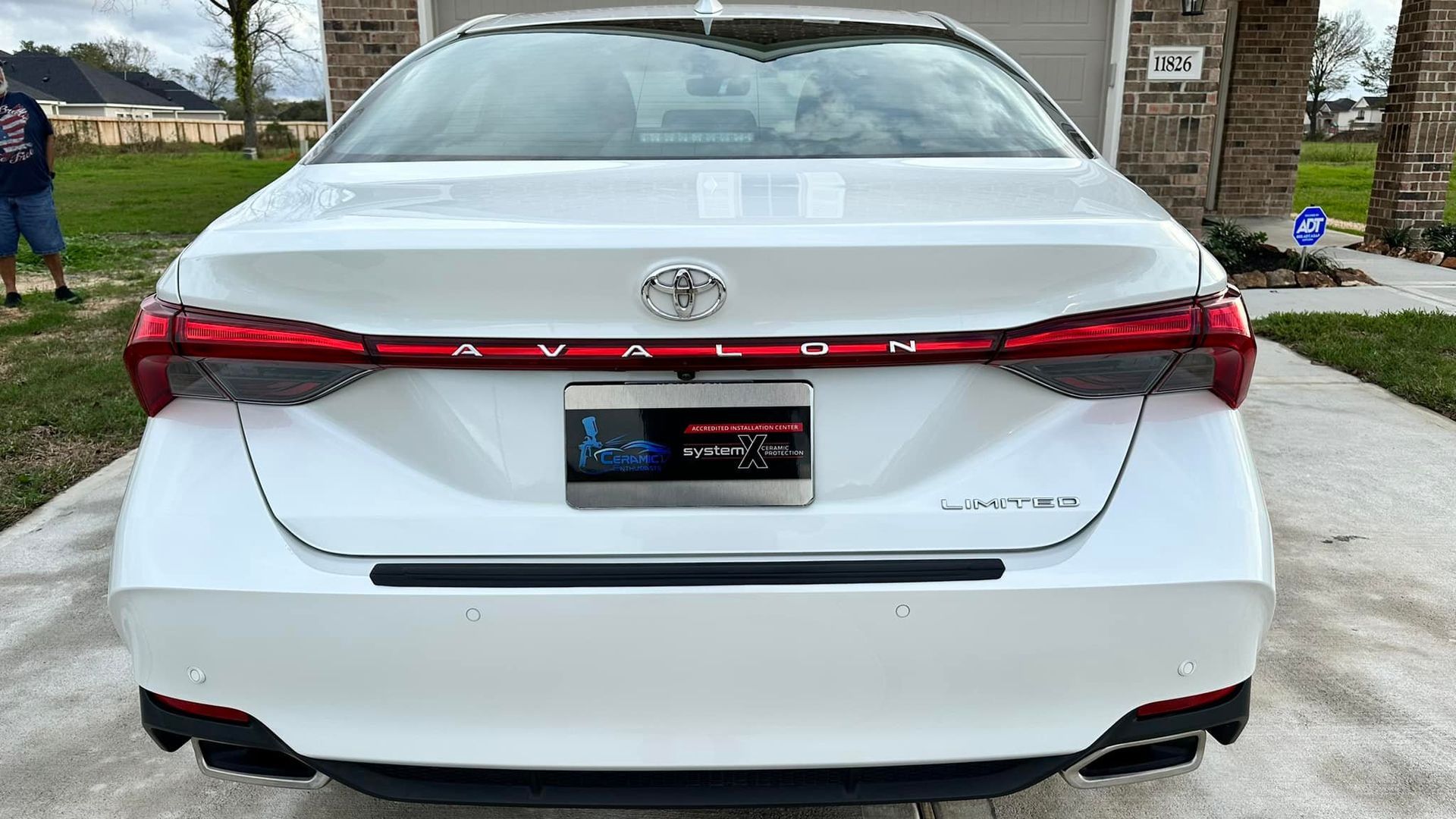 White Toyota Avalon sedan with red taillights and a handicap plate parked on a driveway.