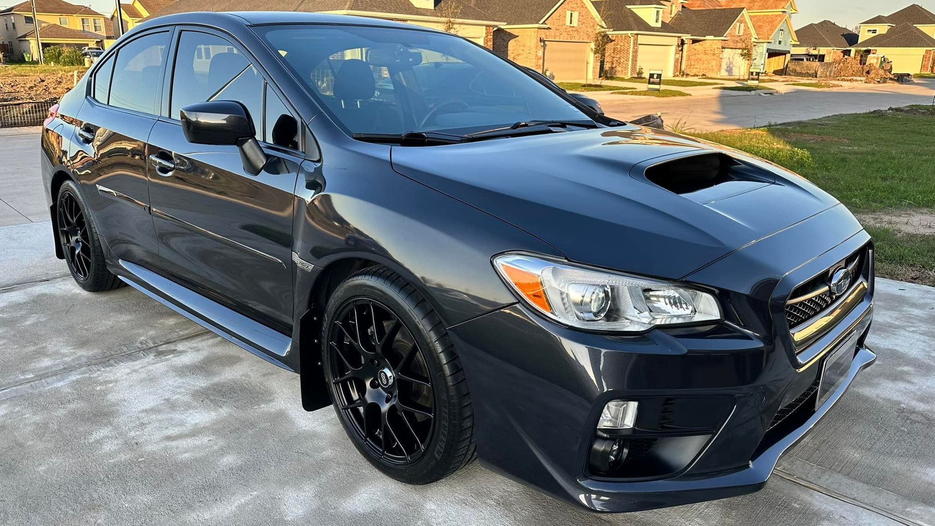 Dark gray Subaru WRX sedan parked on a driveway with black wheels.