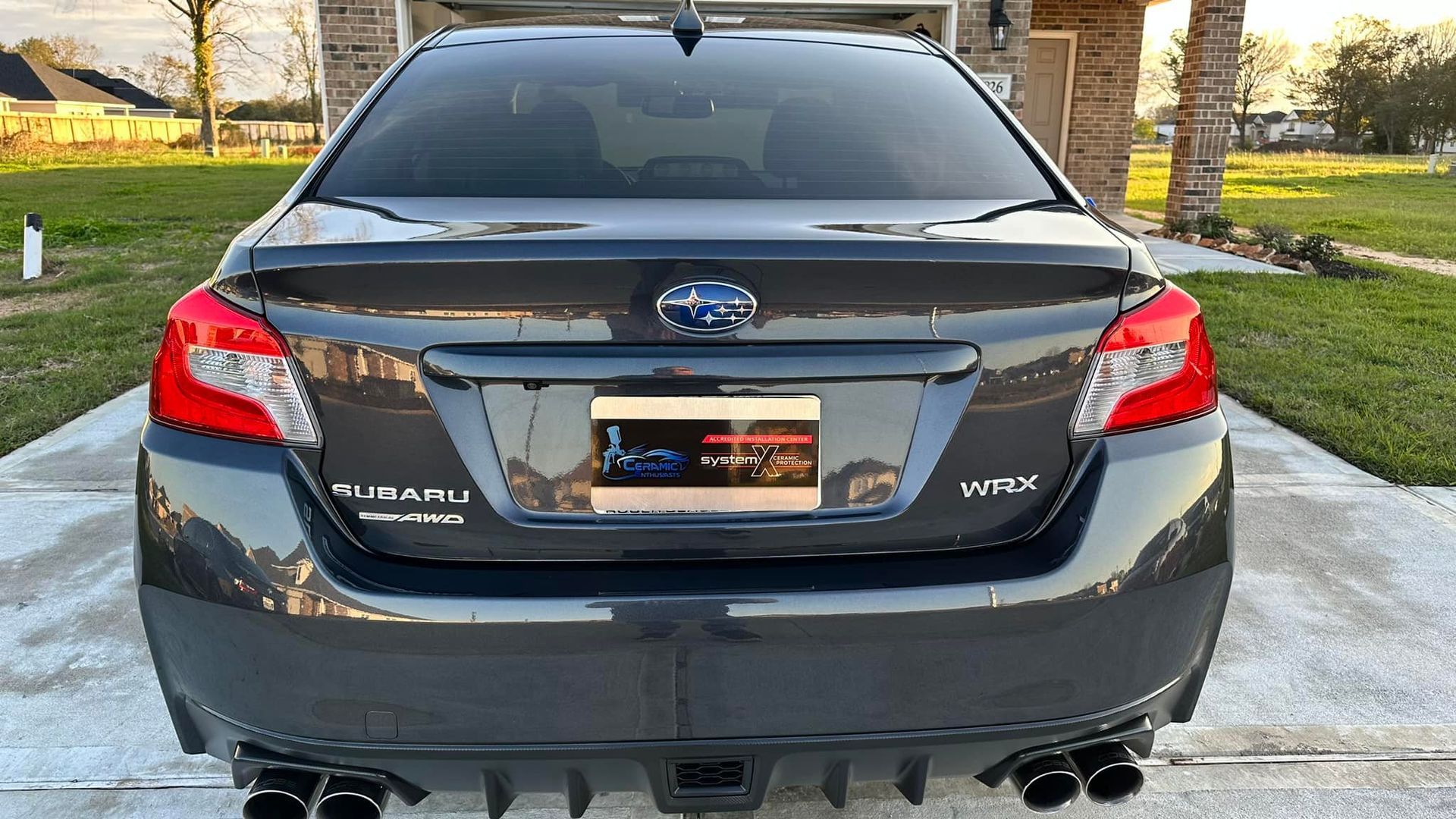 Dark gray Subaru WRX sedan from the rear, exhaust and spoiler visible. License plate and taillights are lit.