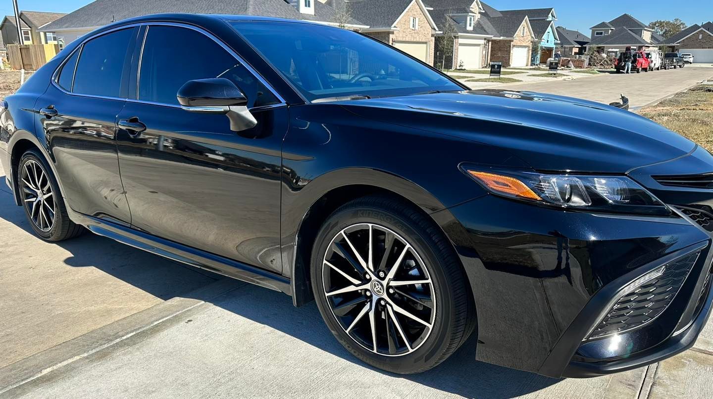 Black Toyota Camry sedan parked on a residential street with tinted windows and sporty wheels.