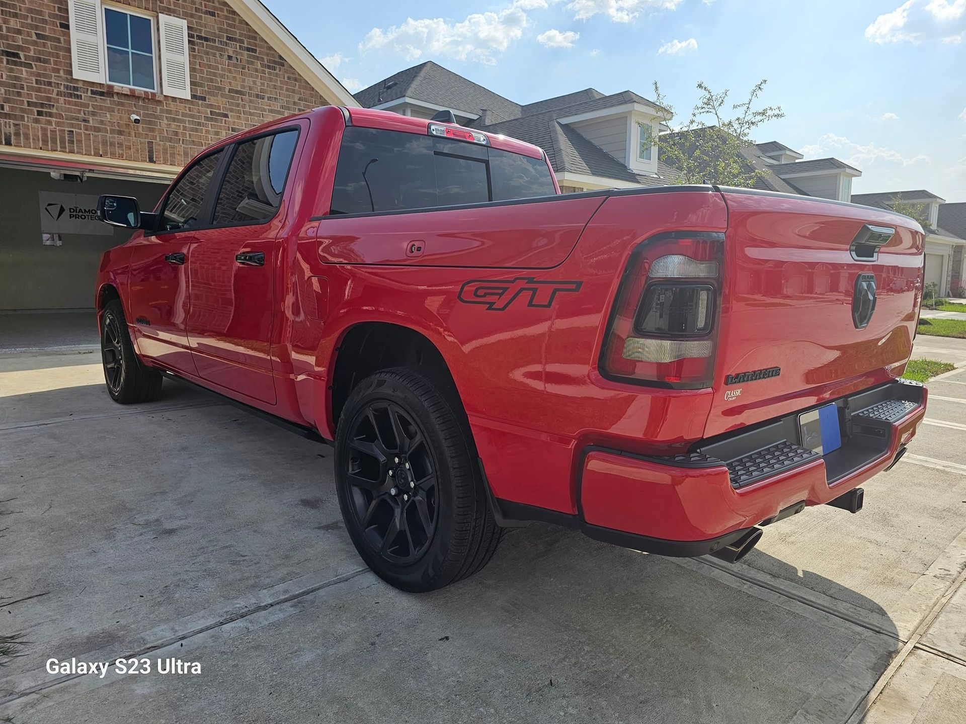 Red Ram 1500 truck parked on a driveway in front of a house on a sunny day.