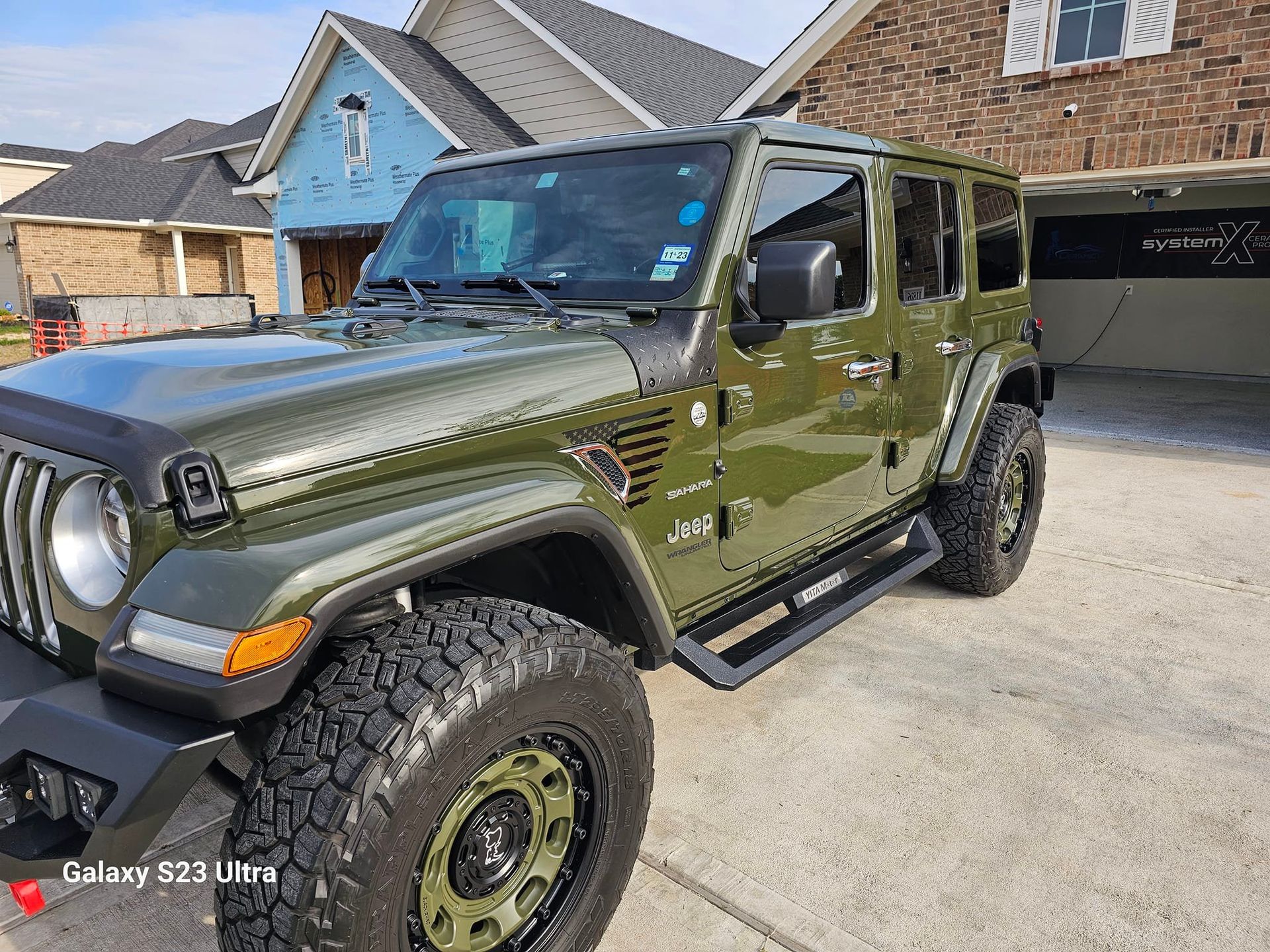 Green Jeep Wrangler parked in front of a house under construction.