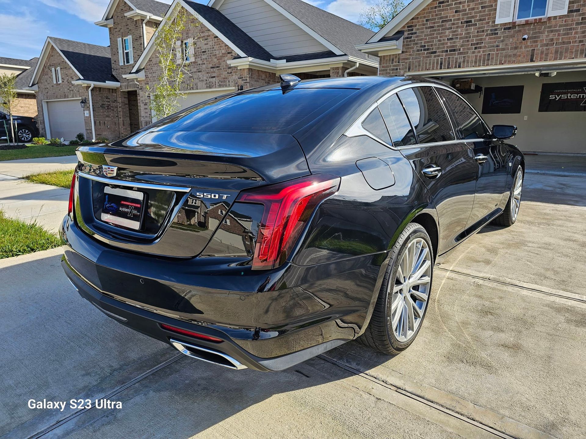 Black Cadillac sedan parked on a driveway in front of a house. Shiny, reflective exterior.