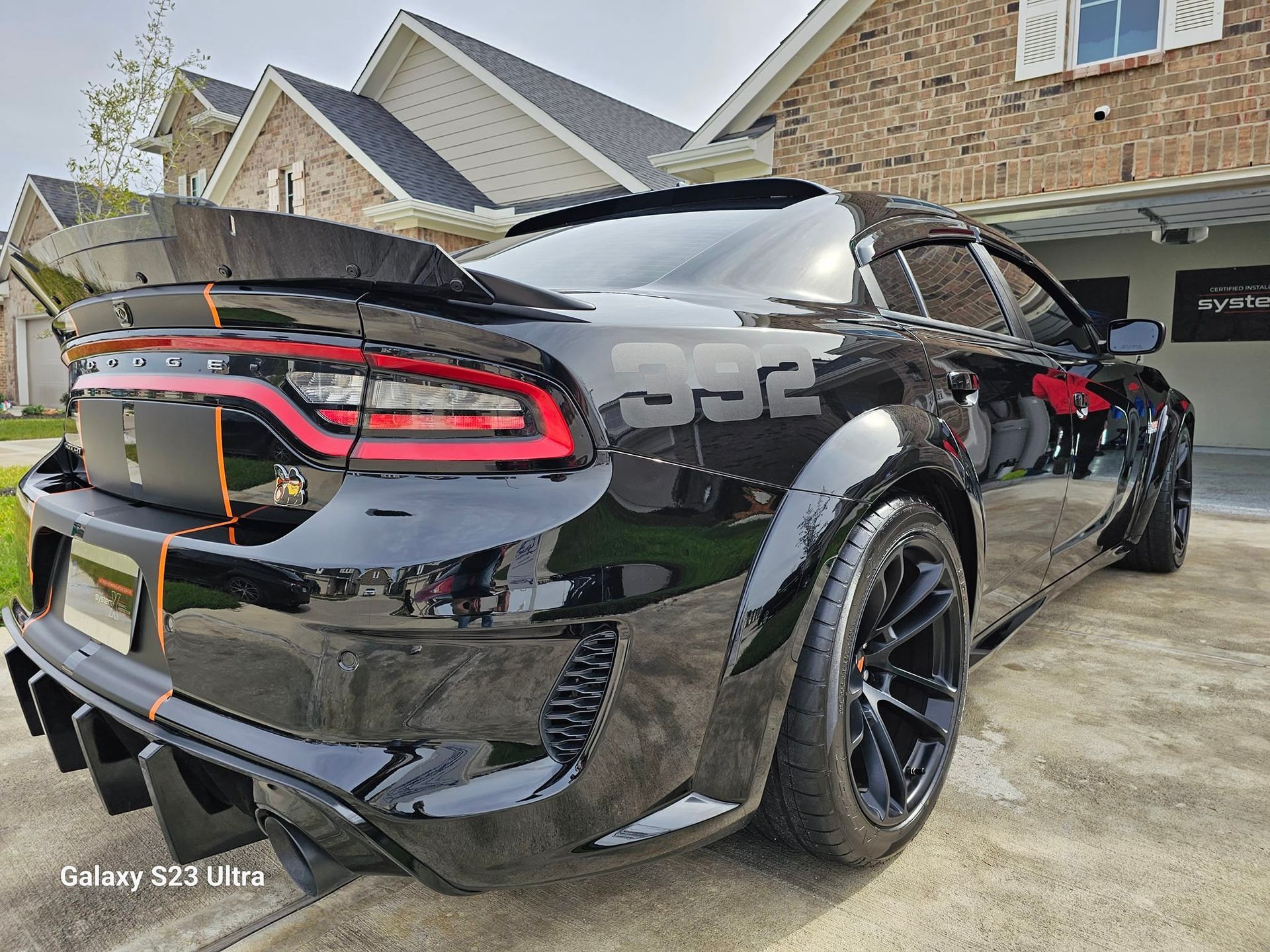 Black Dodge Charger with spoiler and widebody kit parked in front of a house.