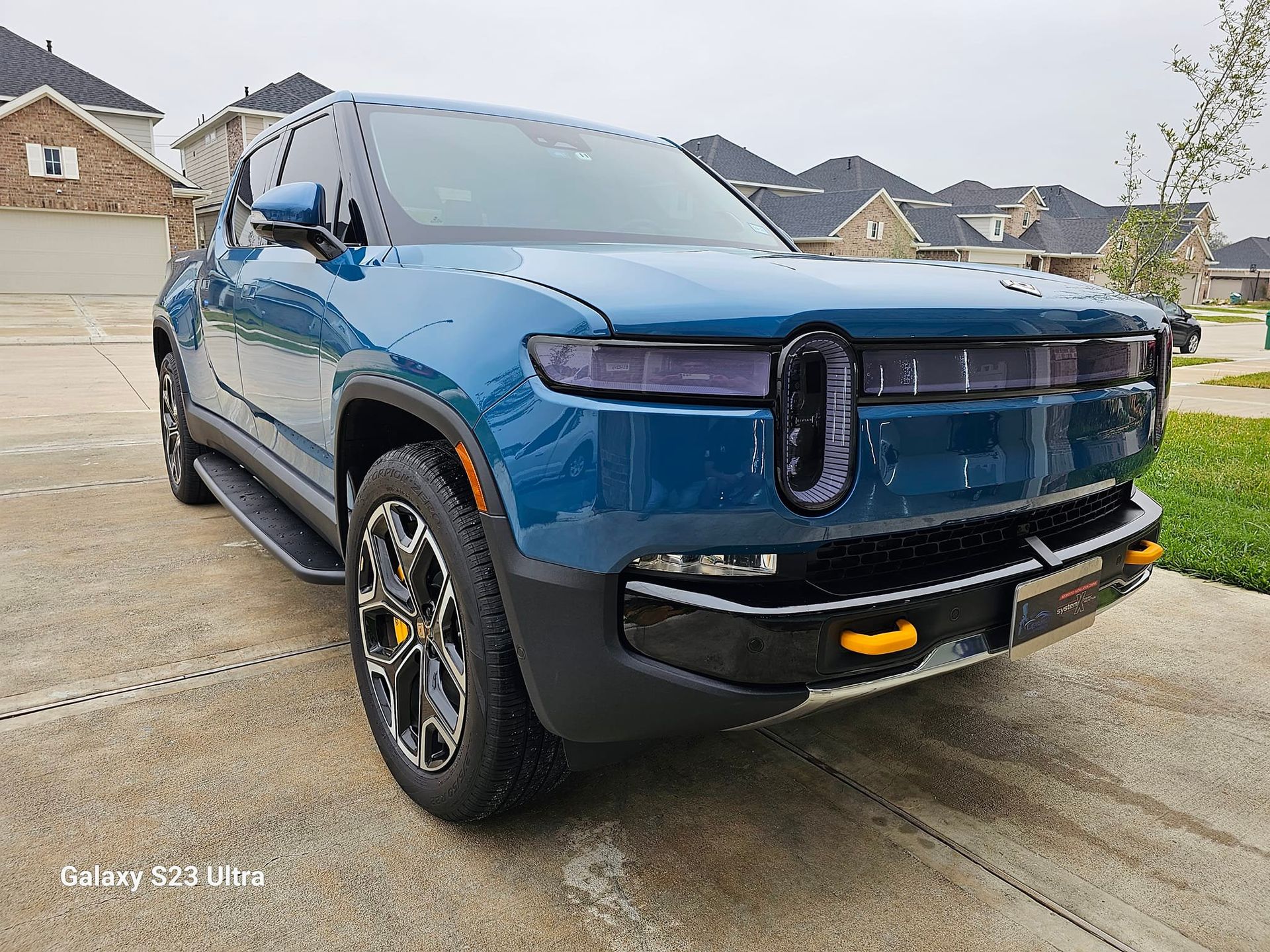 Blue Rivian electric pickup truck parked in a driveway, front view.
