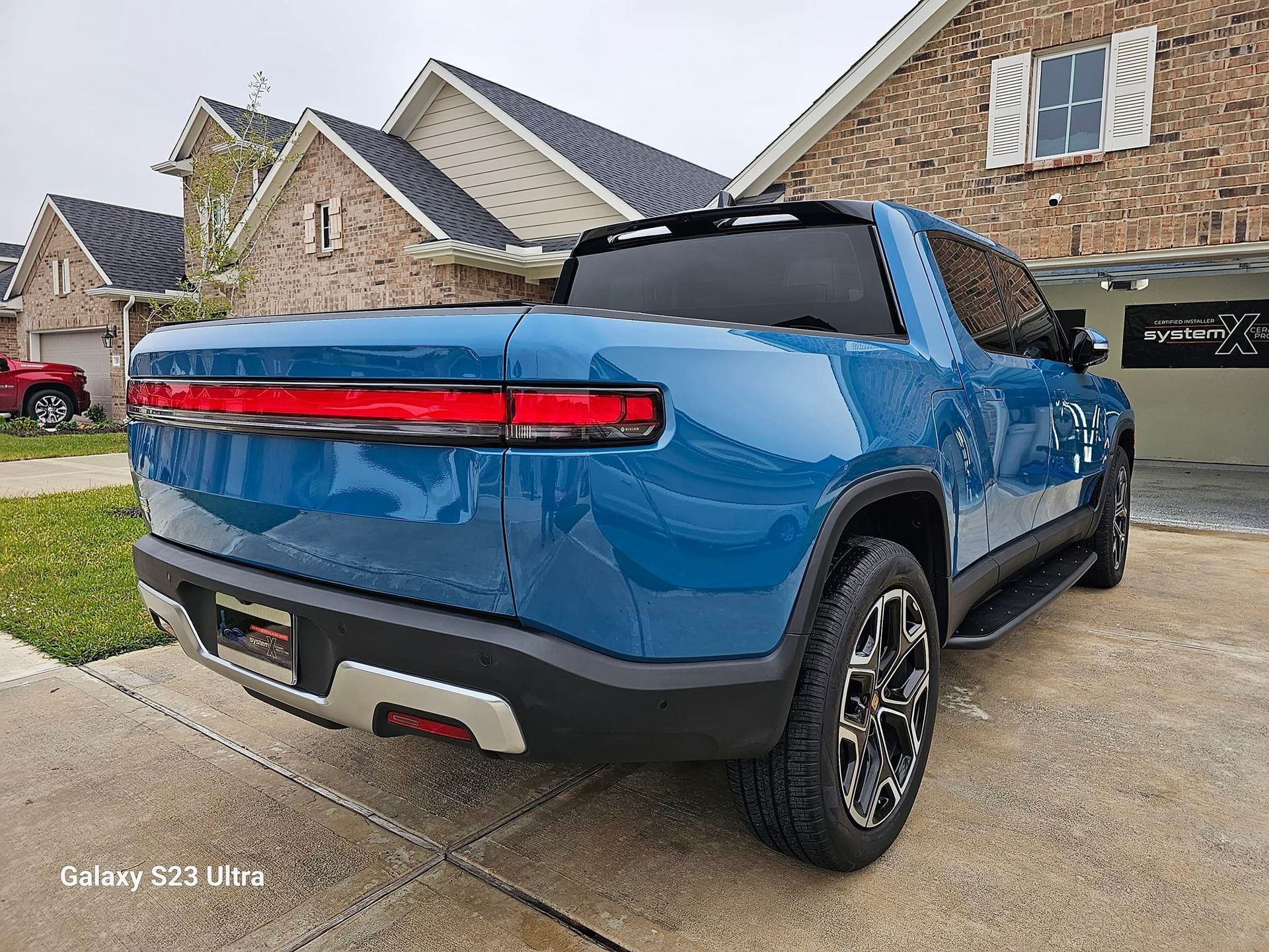 Blue Rivian electric pickup truck parked in front of a house.