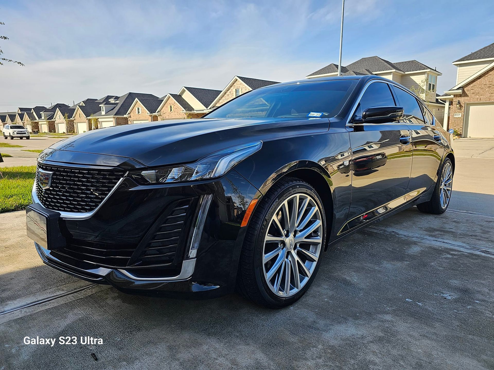 Black Cadillac sedan parked on a driveway in a residential neighborhood on a sunny day.