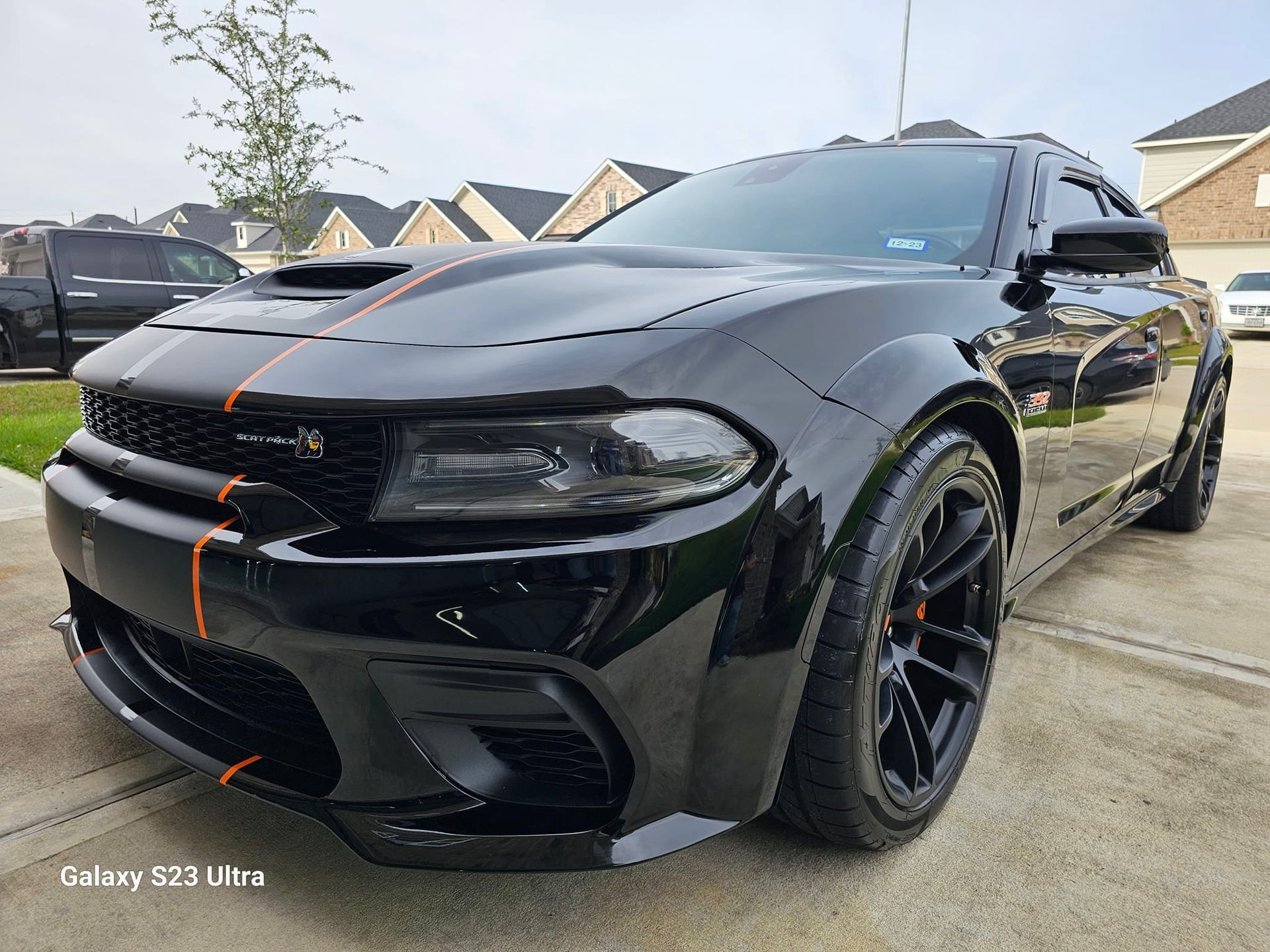 Black Dodge Charger with orange stripes parked in front of a house.