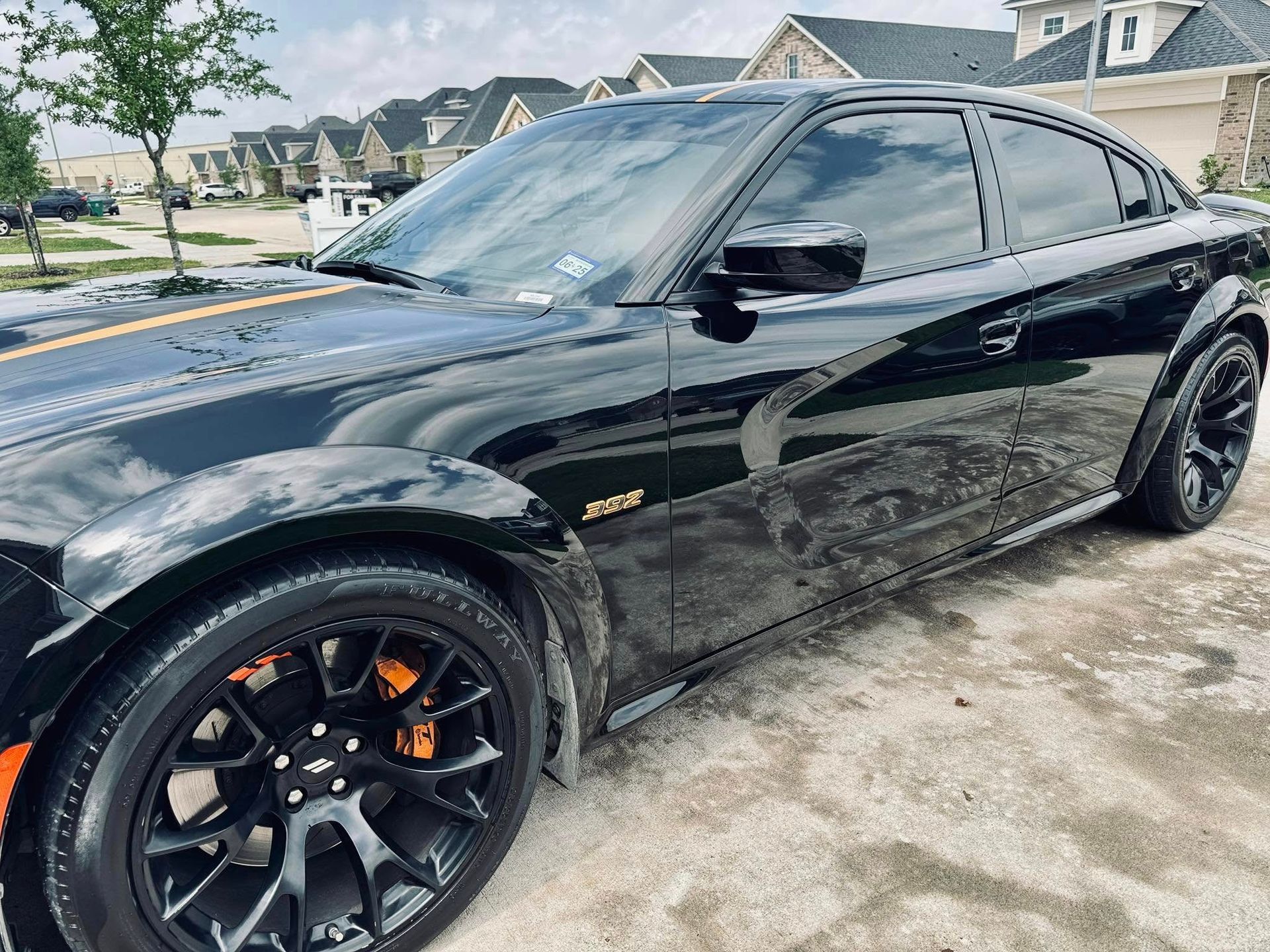 Black Dodge Charger with orange accents parked on a paved driveway; residential neighborhood background.
