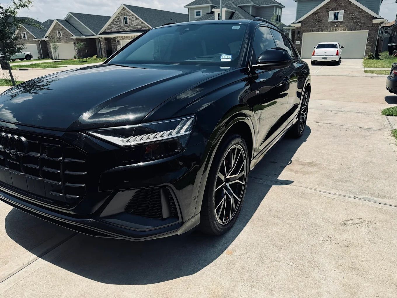 Black Audi Q8 SUV parked on a driveway in front of houses on a sunny day.