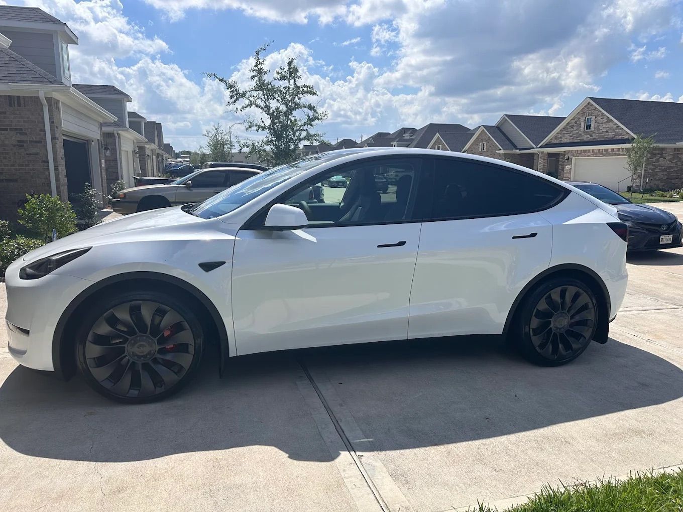 White Tesla Model Y parked in a driveway on a sunny day.