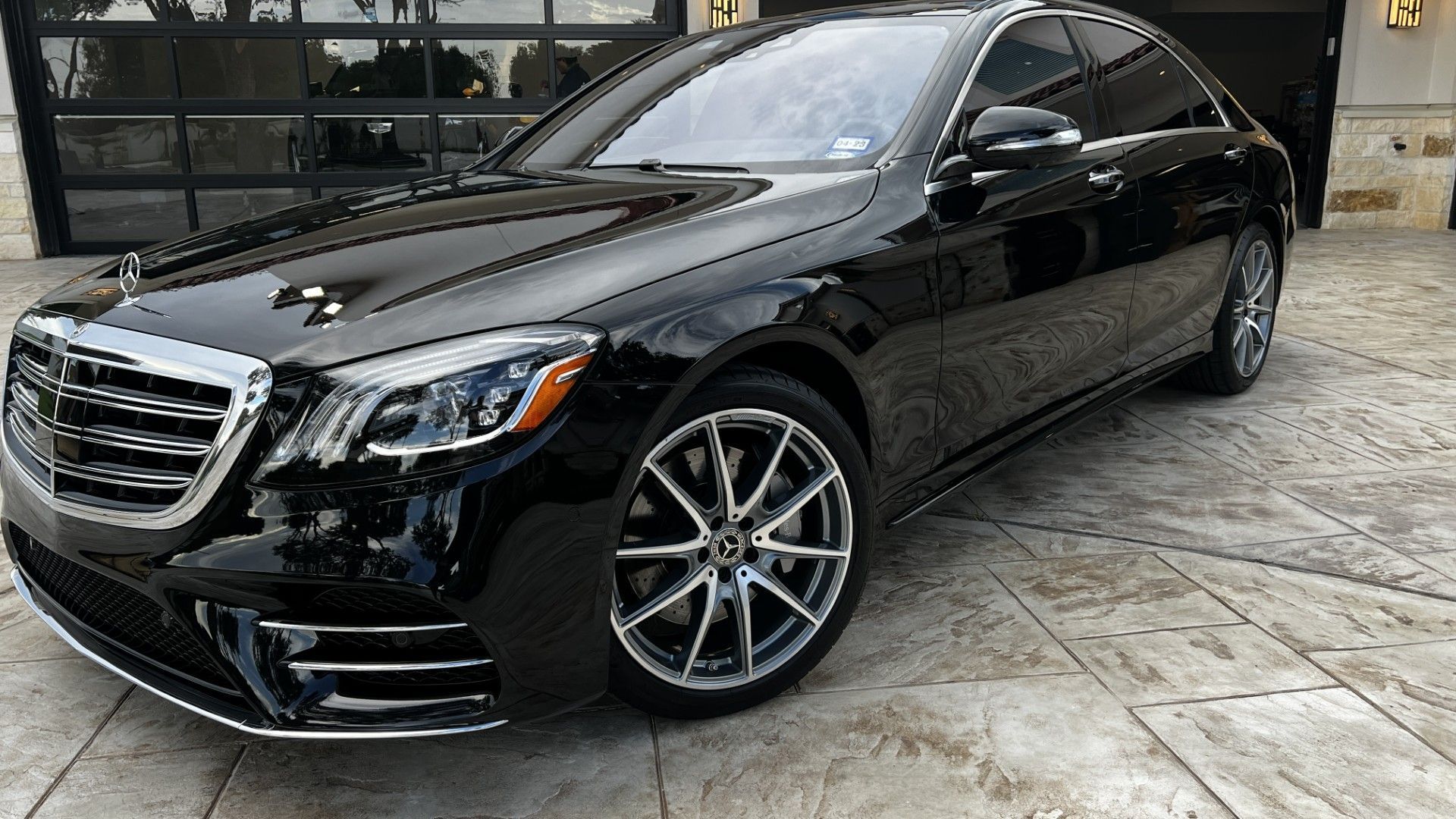 Black Mercedes-Benz sedan parked on a stone driveway, with a glass garage in the background.