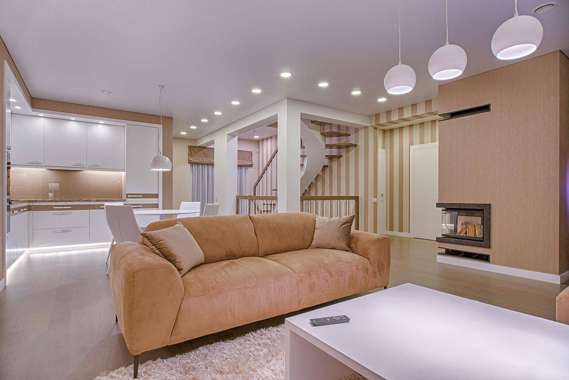 Cozy living room with tan sofa, white table, fireplace, and spiral staircase.