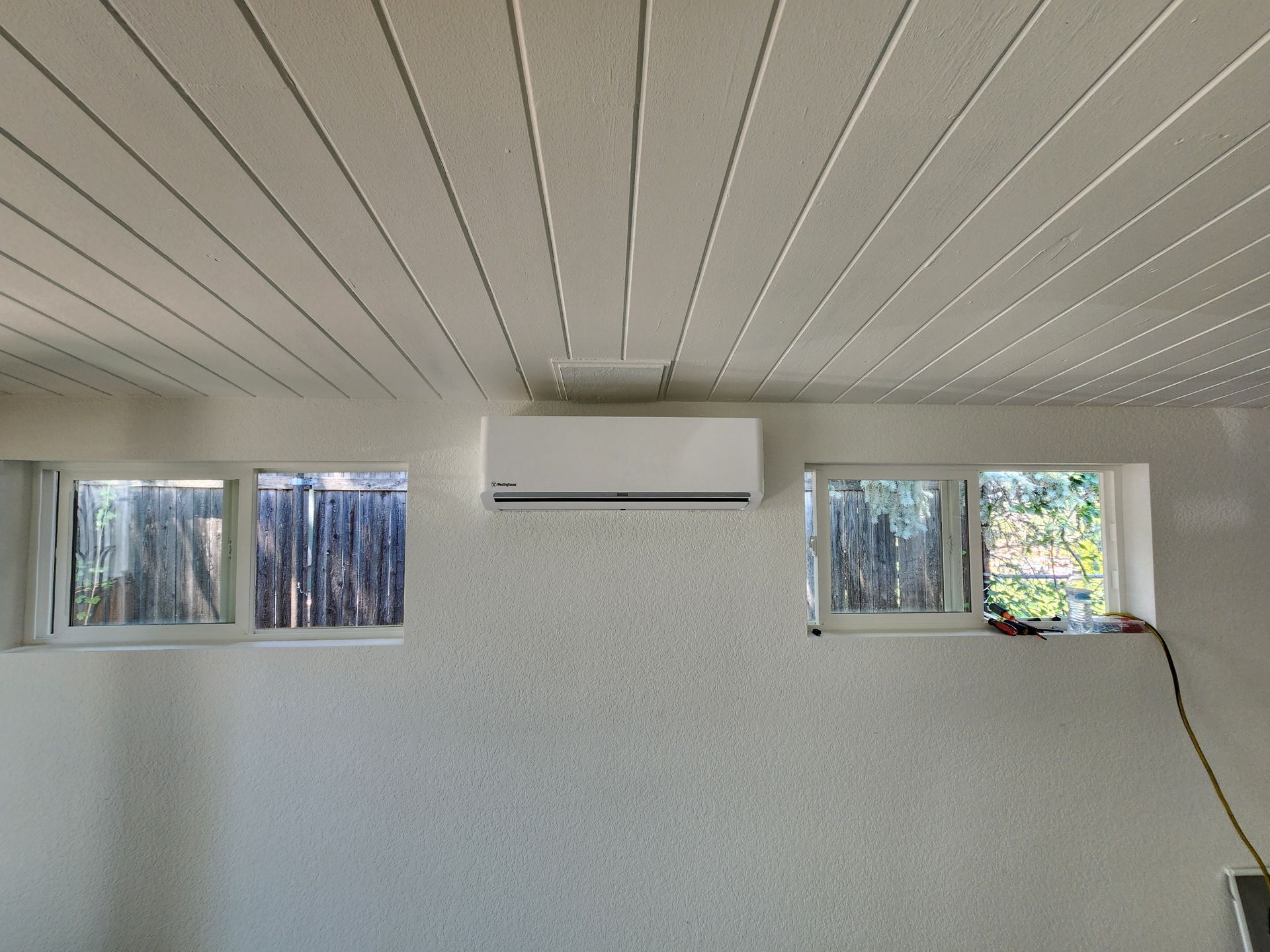 White wall with two windows and a mounted air conditioner. Horizontal panel ceiling.
