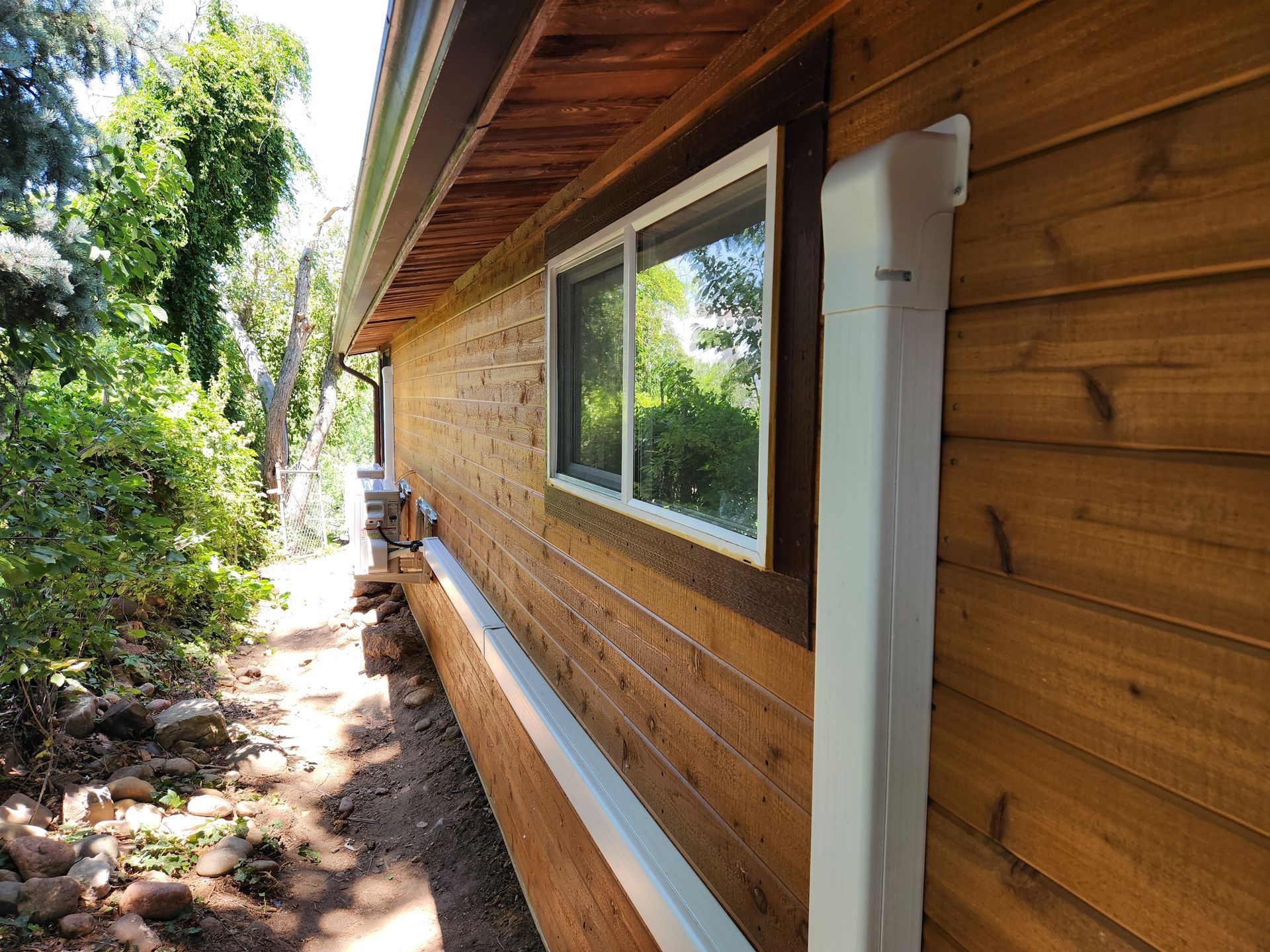 Exterior of a wooden building with a window, white rain gutter, and surrounding trees.