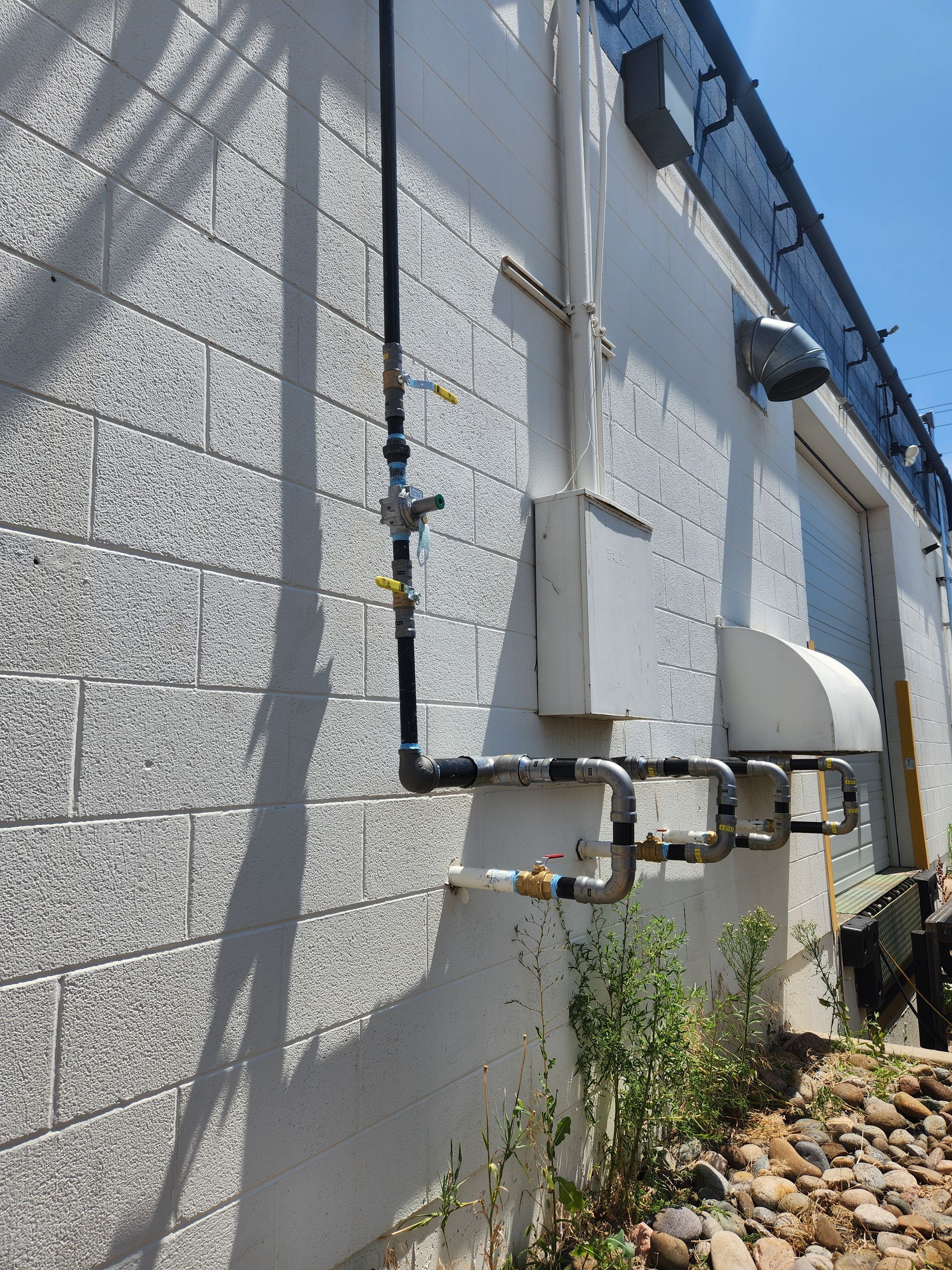 Black pipes and fittings attached to a light-colored brick building.
