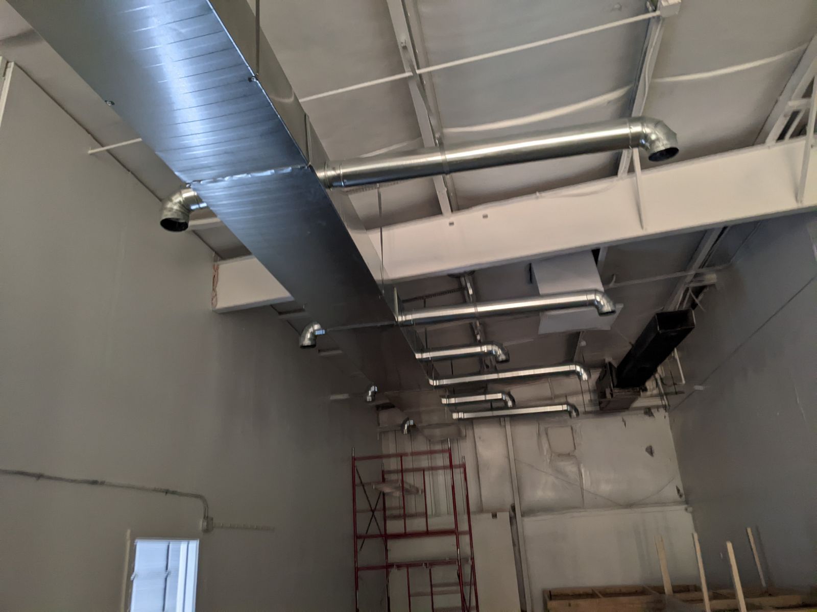 HVAC ductwork installation in a commercial space, with exposed ceiling beams and drywall.