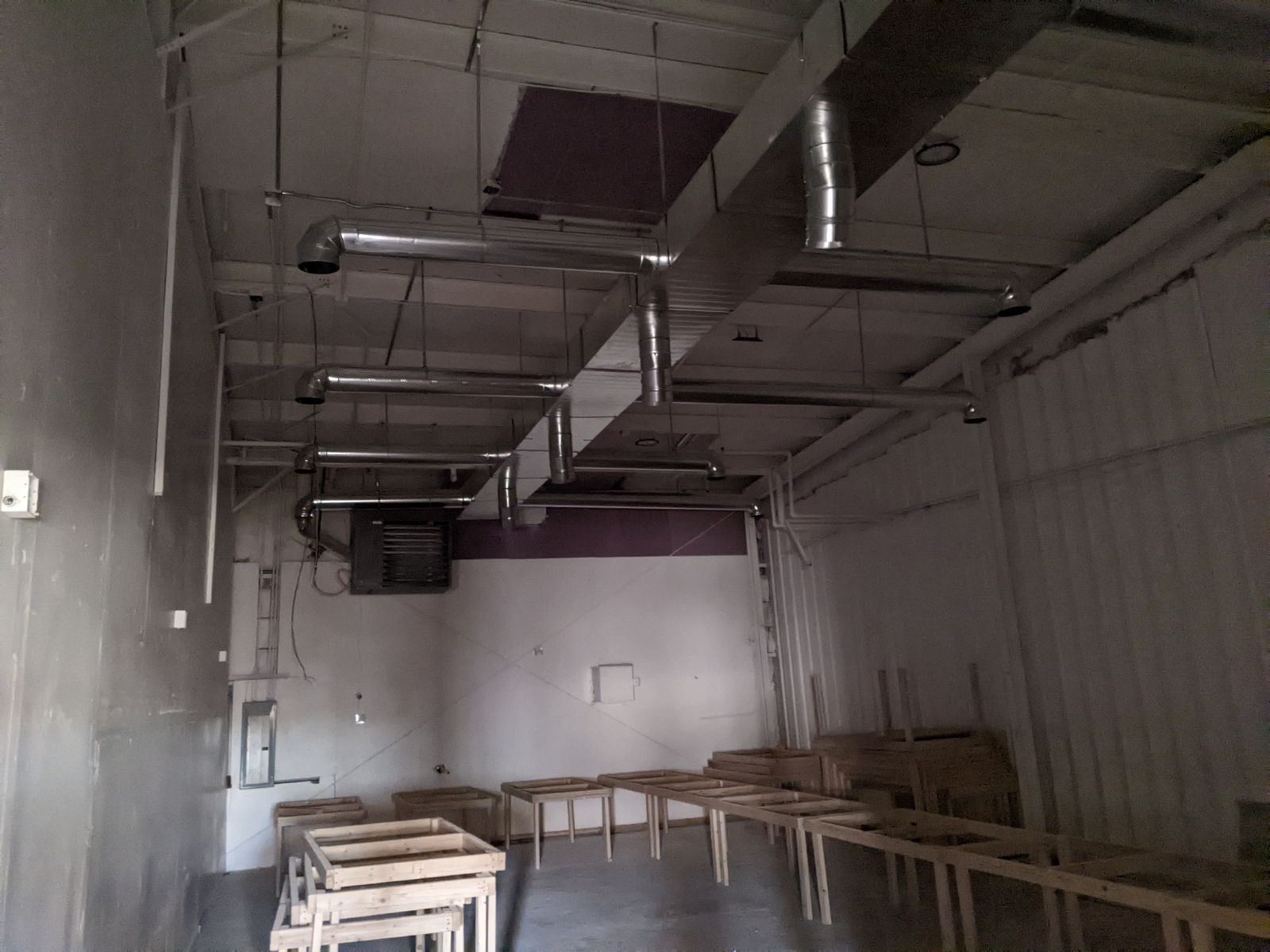 Interior of a room with exposed ductwork on the ceiling and wooden tables.