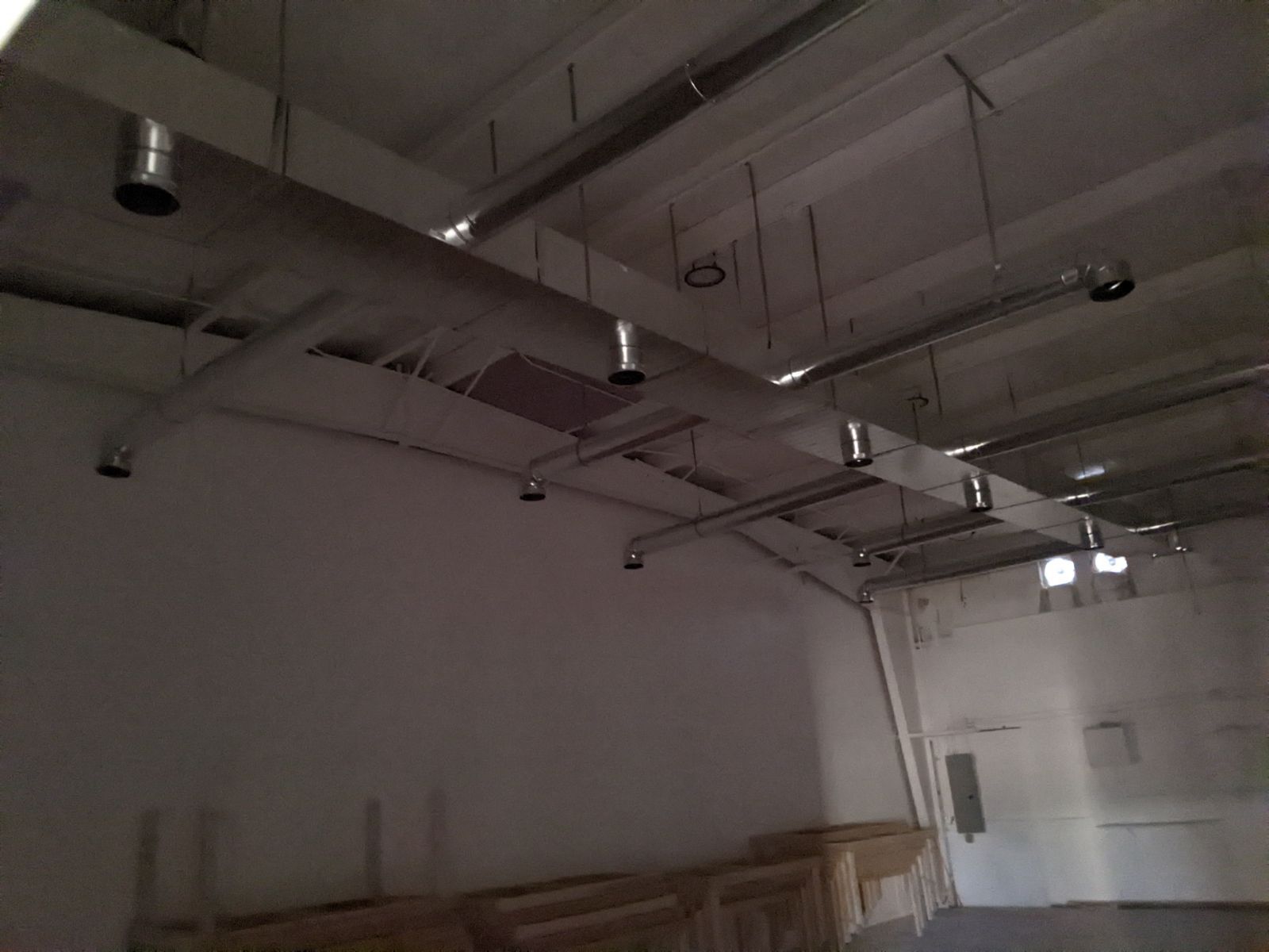 Empty industrial interior with exposed ceiling ductwork and white walls.
