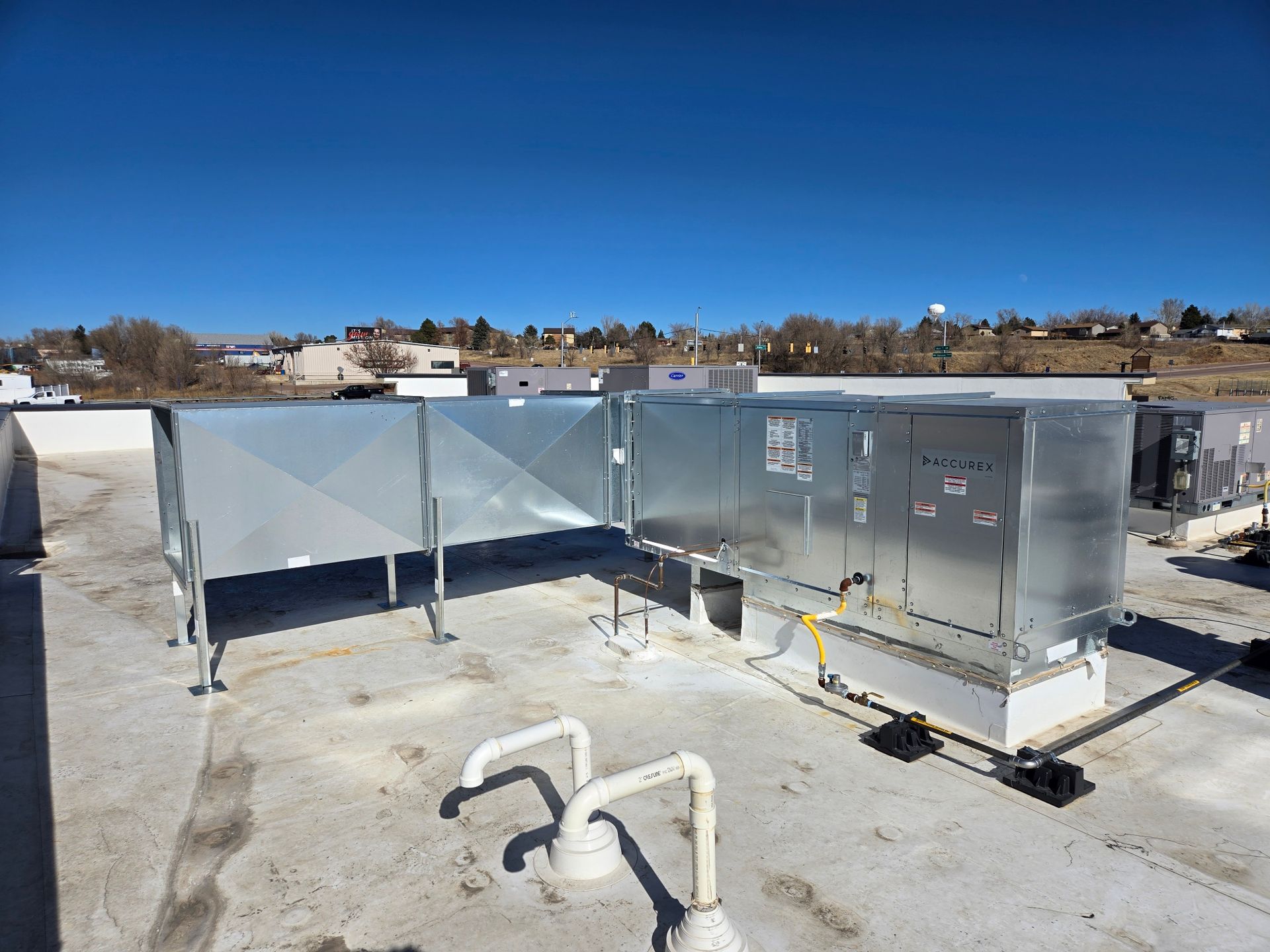 HVAC rooftop unit on a flat roof under a blue sky, with ventilation ducts and piping.