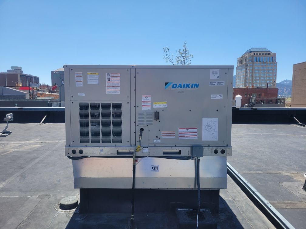 A Daikin rooftop HVAC unit on a flat roof with buildings and mountains in the background under a blue sky.