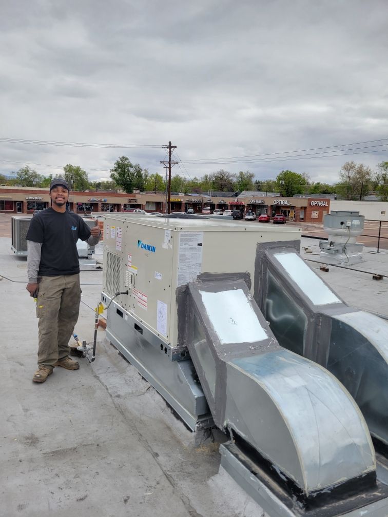 Man standing on a rooftop next to a new HVAC unit. Gray skies.
