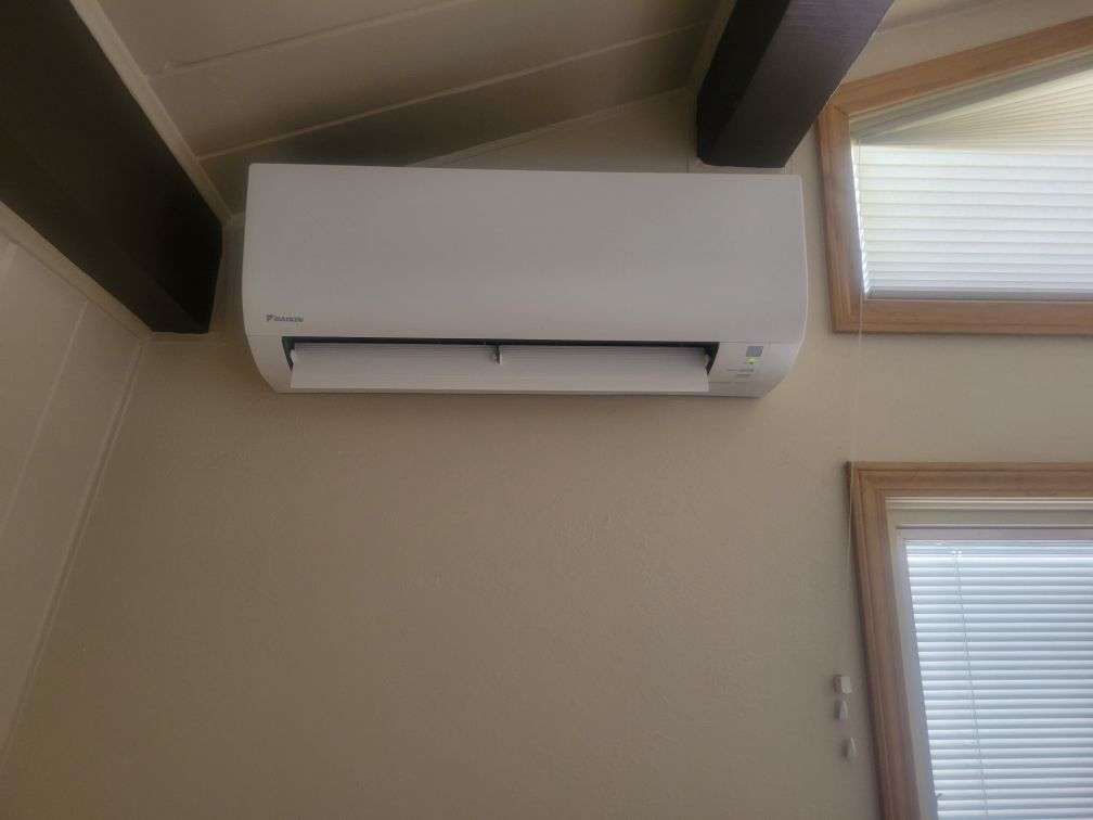 White ductless air conditioner mounted on a beige wall next to a window.