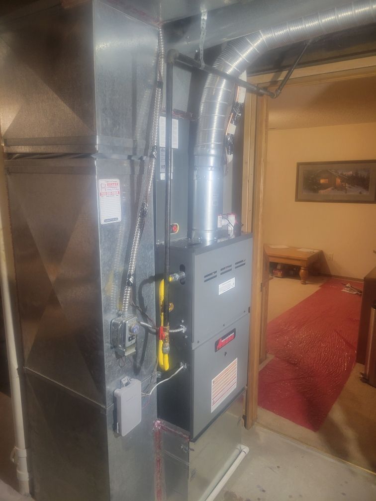 Furnace system in a basement. The unit is grey with silver vents and pipes.