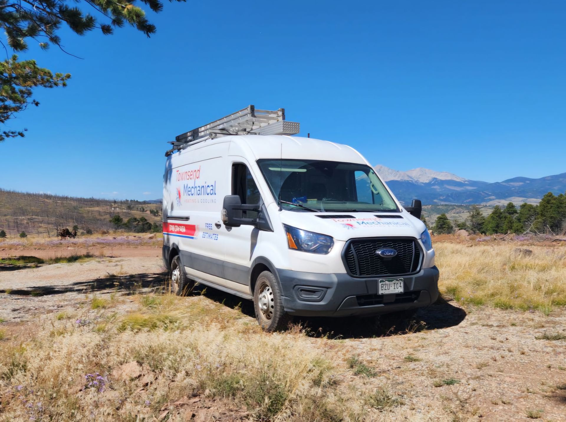 White work van parked on a dirt road in a natural setting, with mountains in the background under a blue sky.