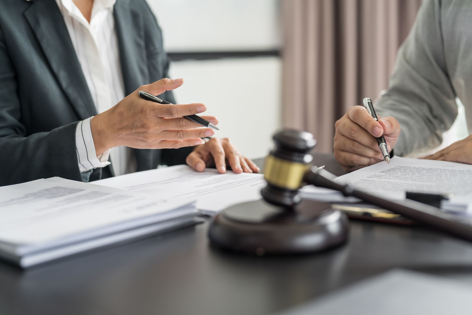 Lawyer pointing at documents, while client signs; gavel on desk.