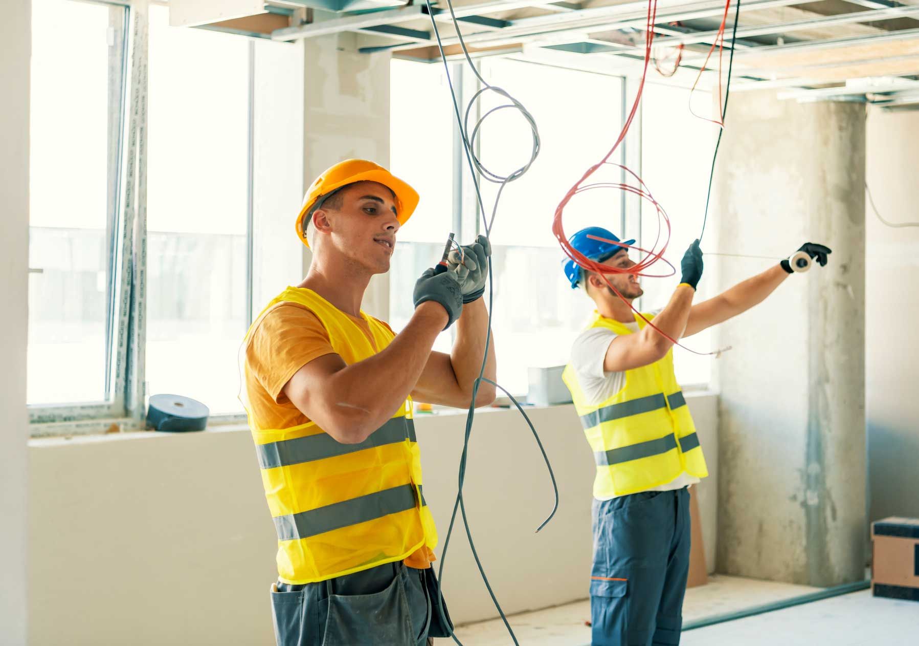 Two construction workers are working on the ceiling of a building.