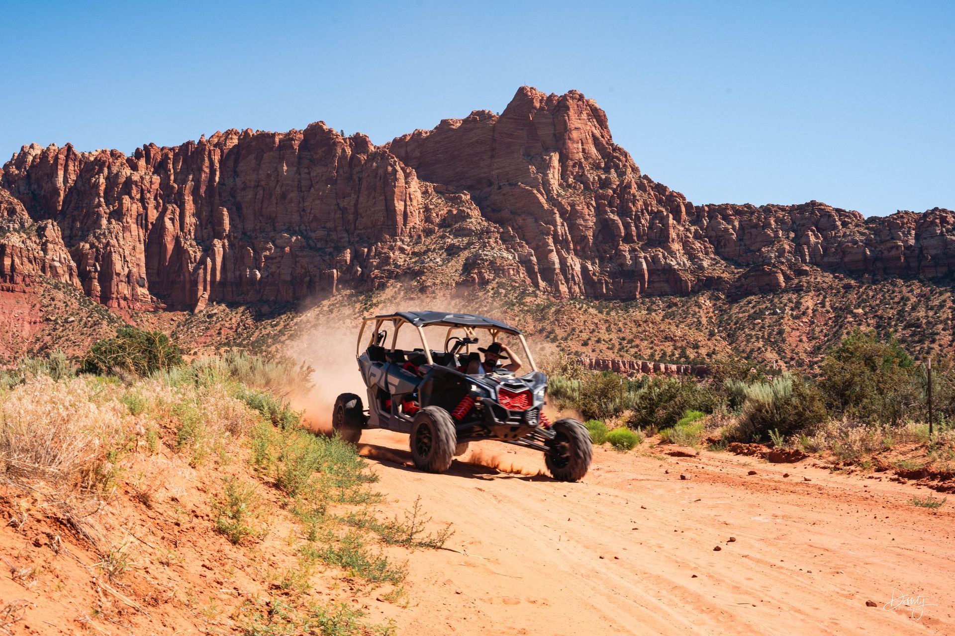 A view from an ATV driving on a dirt road through a desert landscape with mountains in the distance.