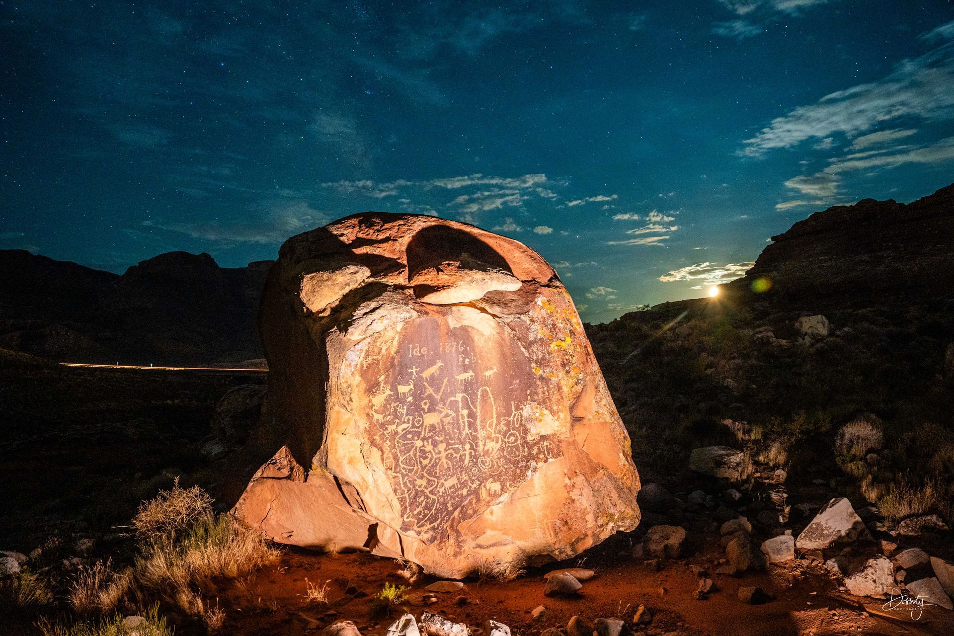 A rock with ancient petroglyphs illuminated under a night sky with stars and moonlight.