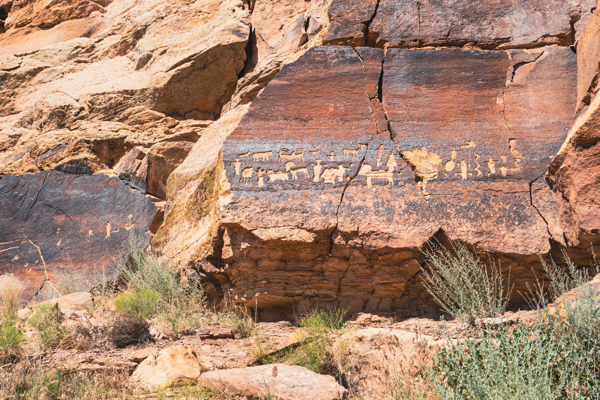 Ancient petroglyphs carved into a rocky cliff face in a desert landscape.