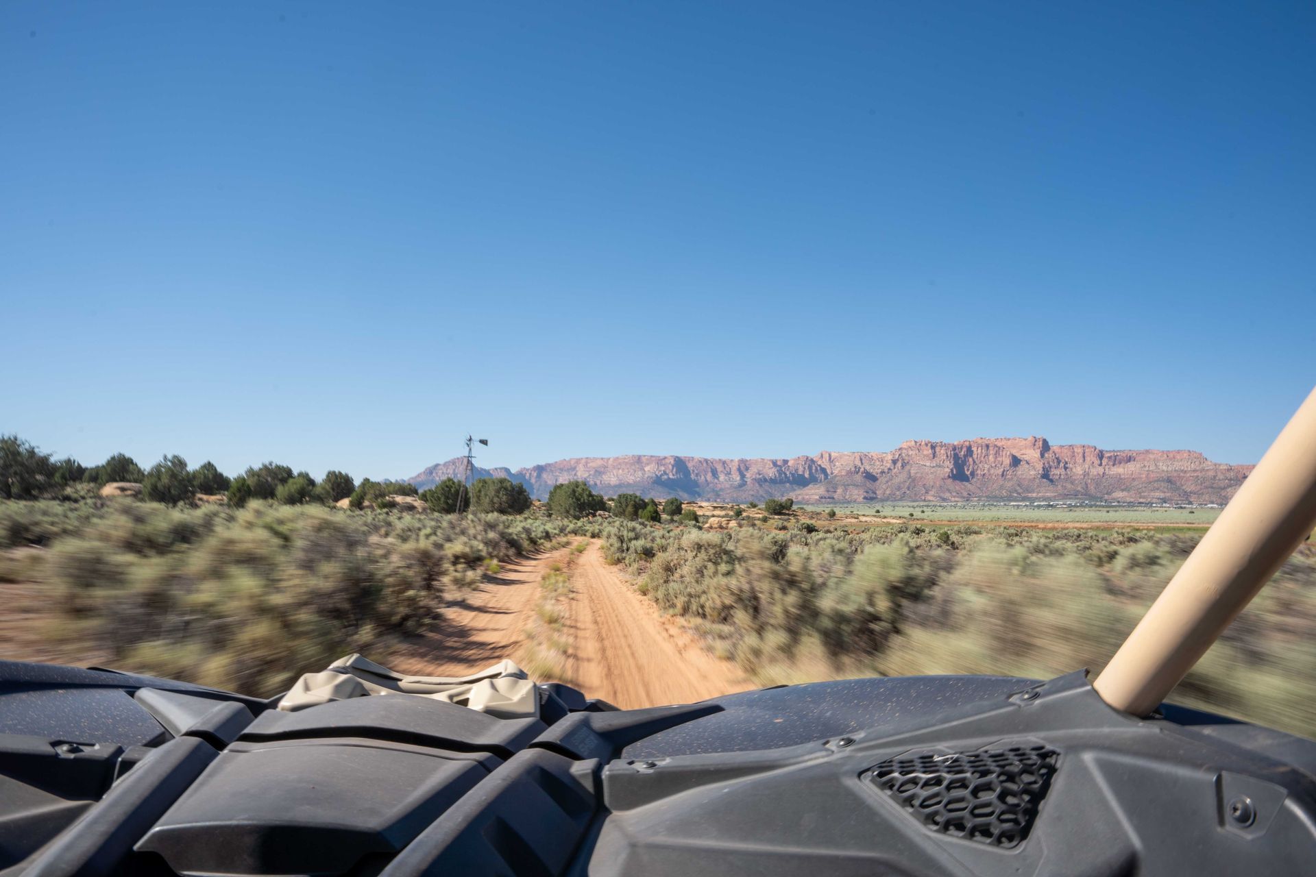 An ATV kicking up dust as it drives along a dirt path in a mountainous desert area.