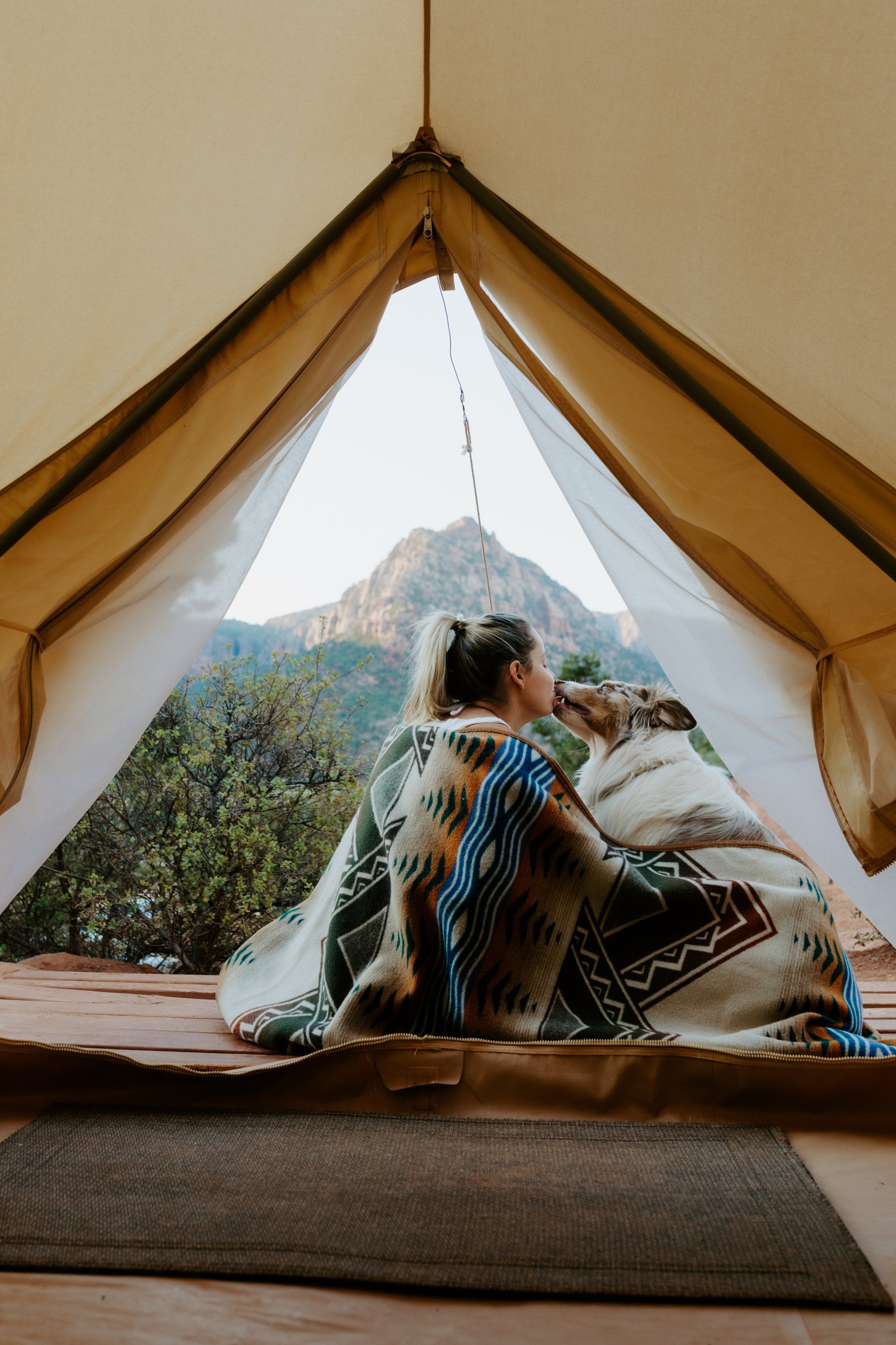 Woman wrapped in a blanket with her dog, enjoying the view from a bell tent at Zion Glamping Adventures.