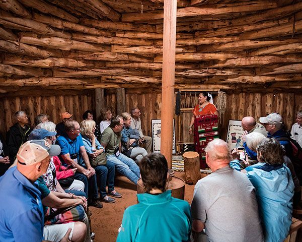 Tourists inside a traditional Navajo hogan, listening to a guide explain cultural heritage and traditions.