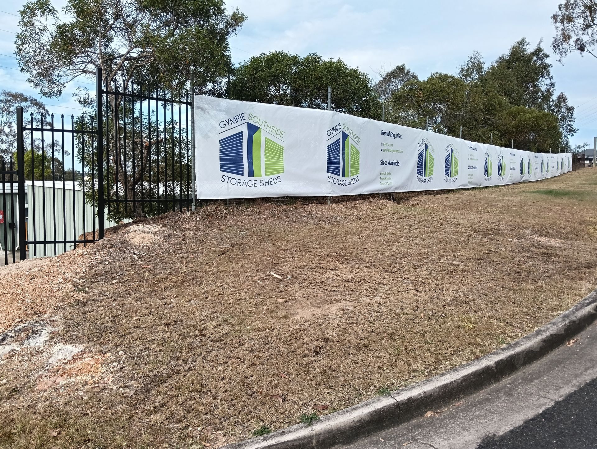 White banner on fence with logo, covering construction site, on a grassy hill — Gympie Southside Mini Storage in Southside, QLD