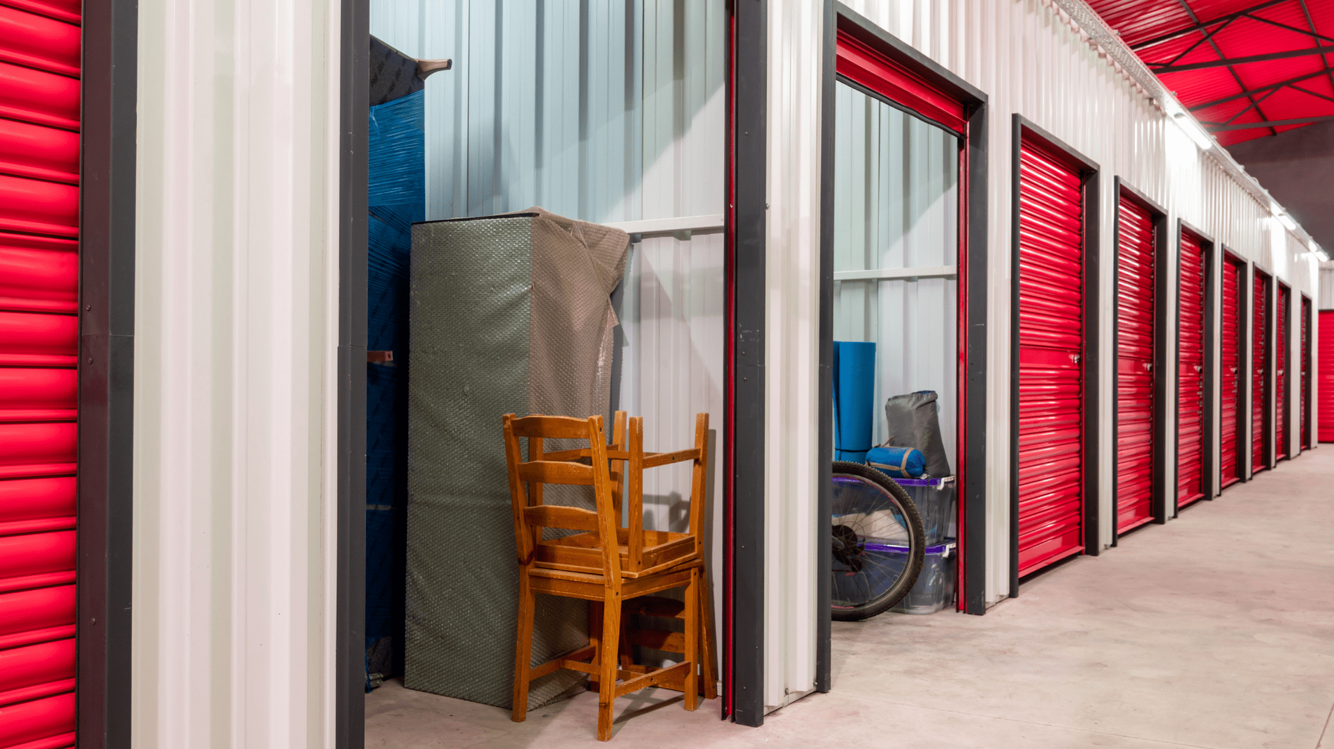Storage units with red doors, interior details of items stored, concrete floor — Gympie Southside Mini Storage in Southside, QLD